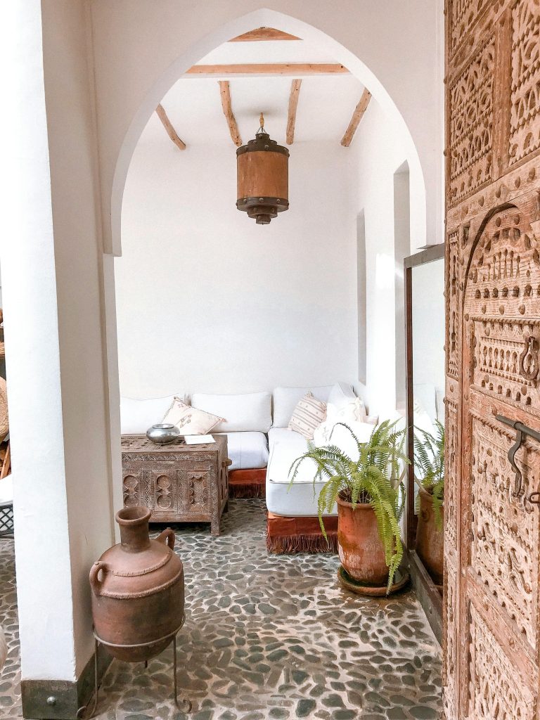 Elegant bohemian Moroccan-style room featuring antique wooden decor and lush greenery for a cozy ambiance.